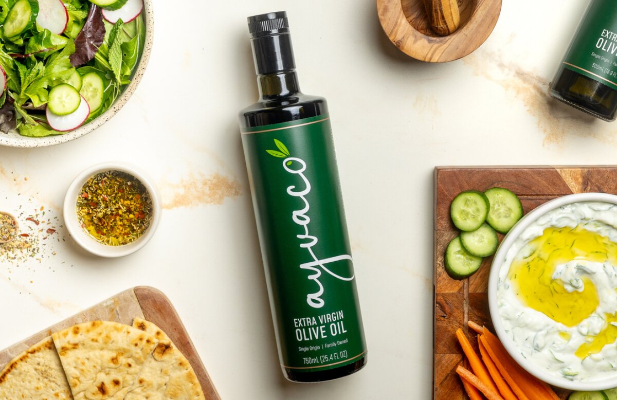 Bottle of Ayvaco Extra Virgin Olive Oil on a table surrounded by food